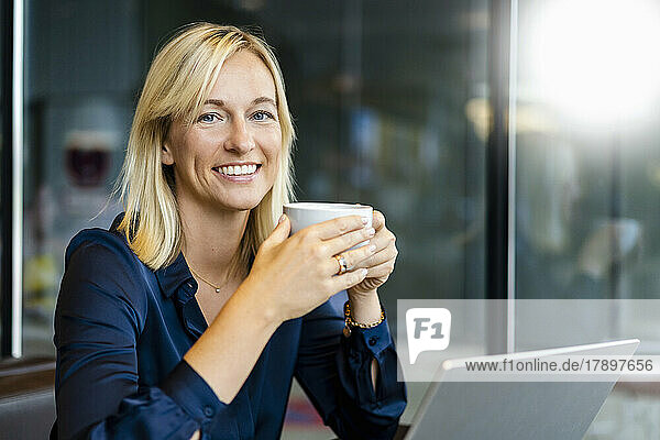 Happy freelancer with coffee cup sitting at cafe