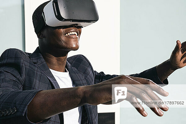 Happy young man wearing virtual reality glasses in front of wall