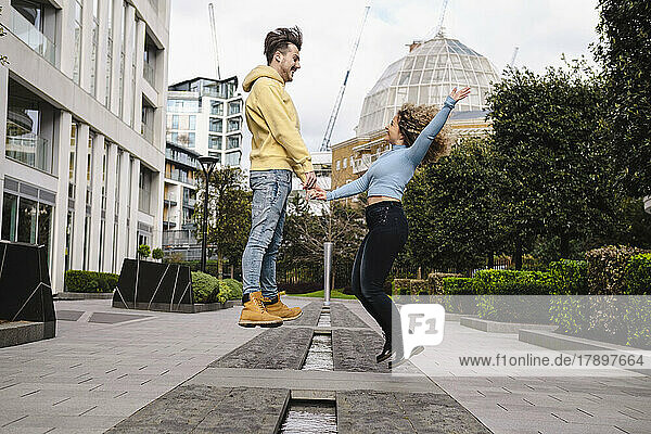 Cheerful young couple jumping together on footpath