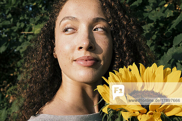 Lächelnde schöne Frau mit Sonnenblume  die das Sonnenlicht genießt