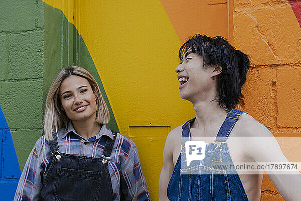 Young friends hanging out with each other standing in front of rainbow painted on wall