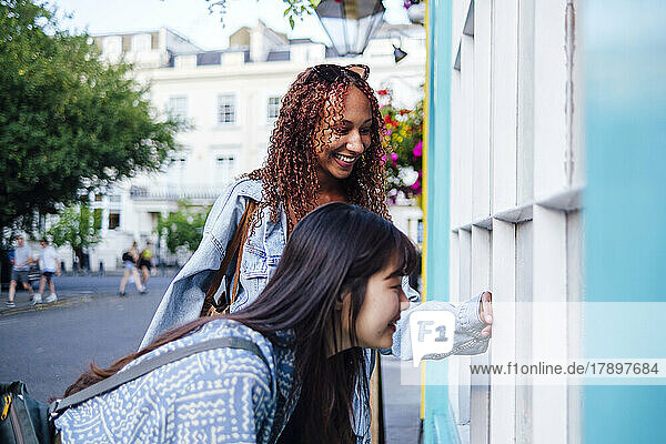 Happy young woman with friend looking through window at footpath