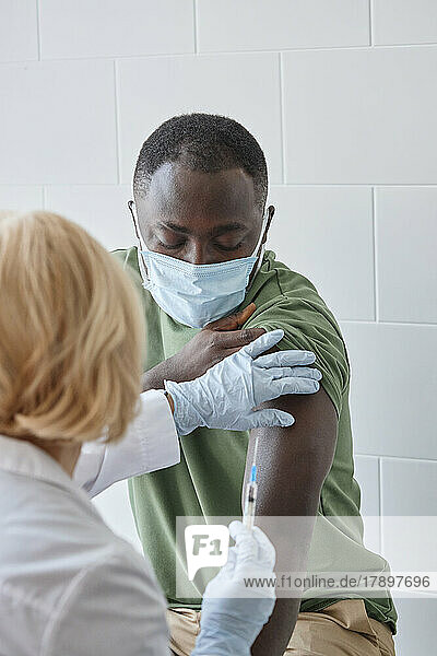 Doctor injecting COVID-19 vaccine on patient arm in clinic