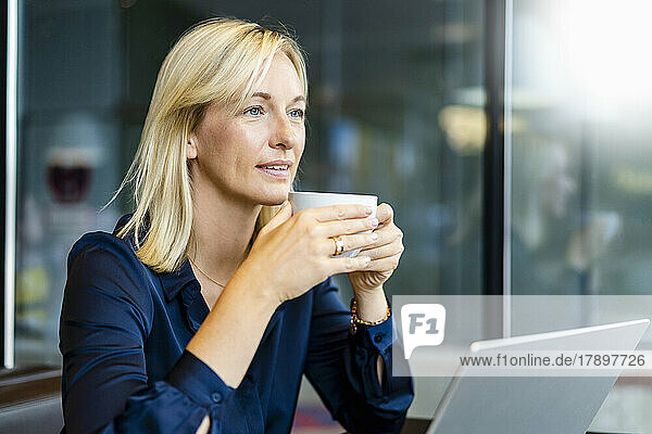 Smiling freelancer with coffee cup sitting in cafe