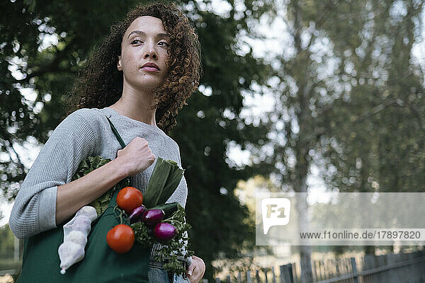Contemplative woman with bag of vegetables walking in park
