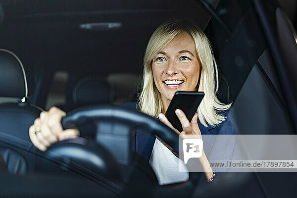 Businesswoman talking on speaker phone driving car seen through windshield
