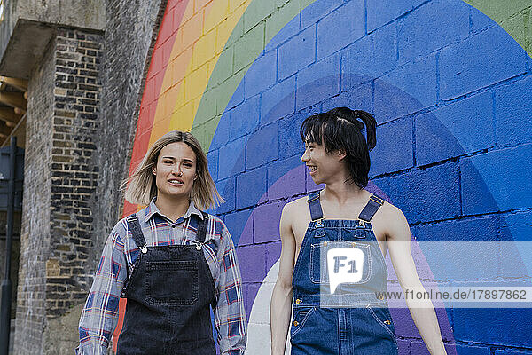 Young friends walking together by rainbow painted on wall