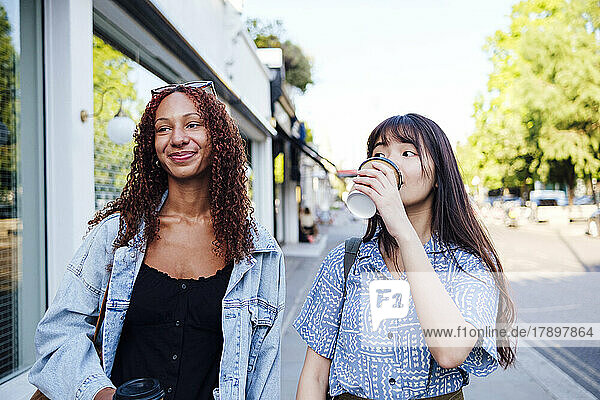 Smiling woman with friend drinking coffee at footpath
