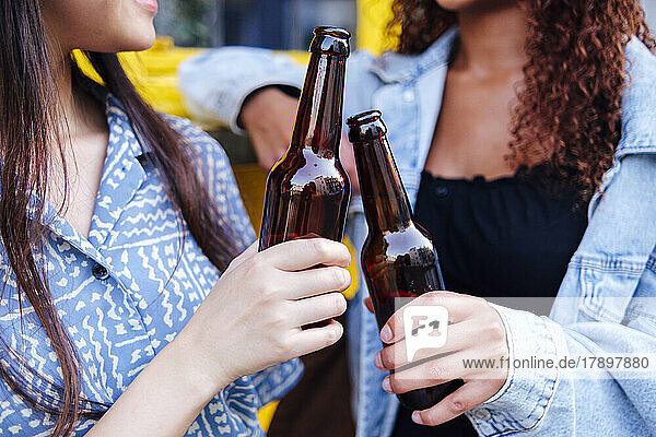 Young woman with friend toasting beer bottles