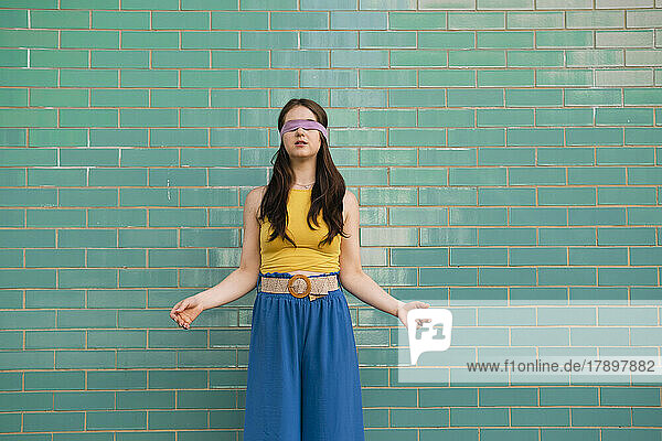 Woman with blindfold standing in front of teal wall