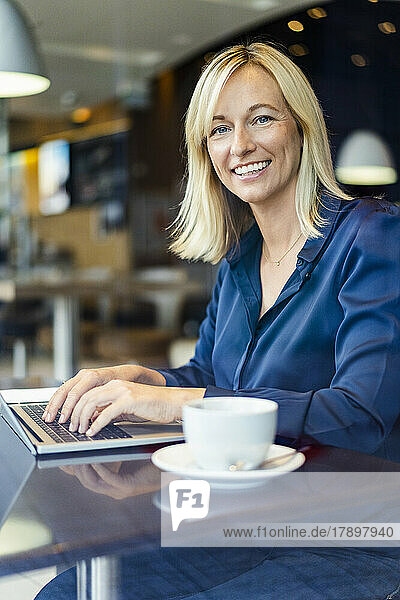 Glückliche Geschäftsfrau mit Laptop sitzt am Tisch im Café