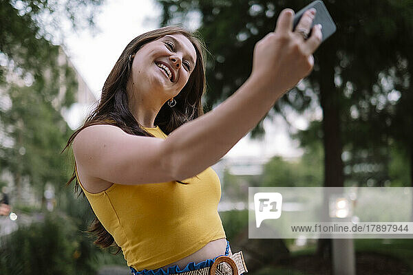 Lächelnde junge Frau  die im Park ein Selfie mit dem Smartphone macht