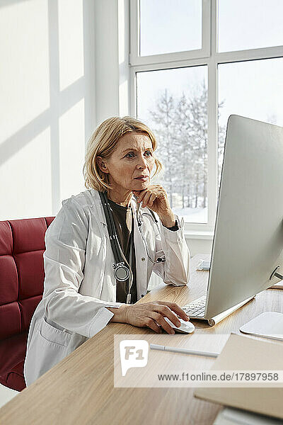 Concentrated doctor working on desktop PC sitting at desk in clinic