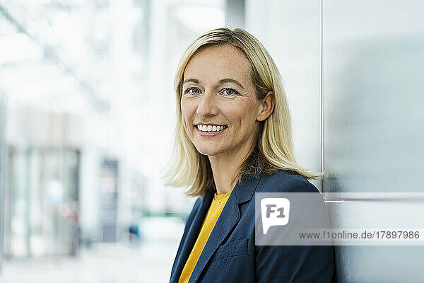Smiling businesswoman with blond hair leaning on wall