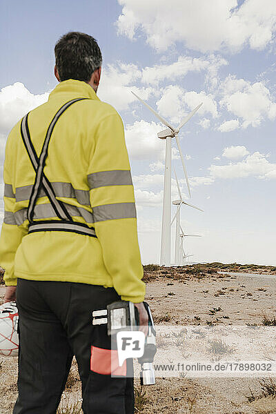 Technician with work tool looking at wind turbines