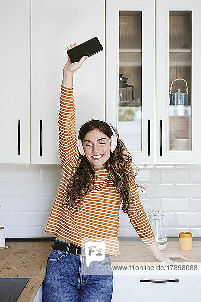 Fröhliche junge Frau  die zu Hause in der Küche mit Kopfhörern Musik hört