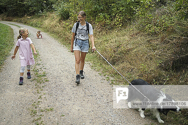 Lächelnde Frau mit Hund und Tochter geht im Wald spazieren