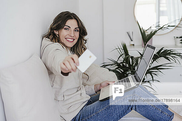 Happy young woman with laptop showing credit card