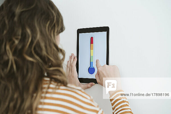 Young woman using digital tablet with thermometer icon on the wall