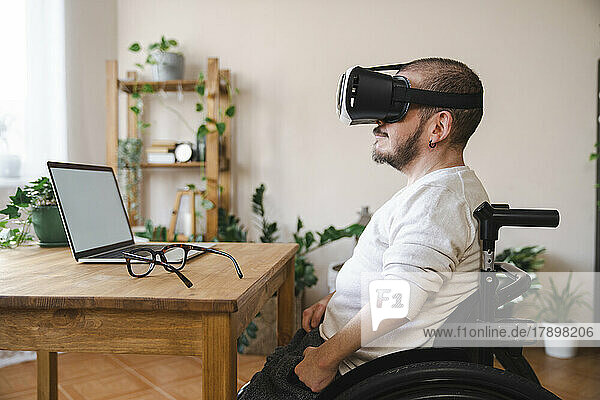 Man with disability wearing virtual reality simulator in front of laptop at home