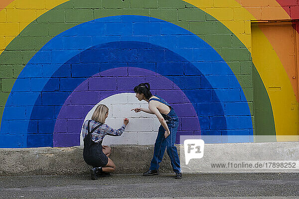 Woman with friend writing on rainbow mural