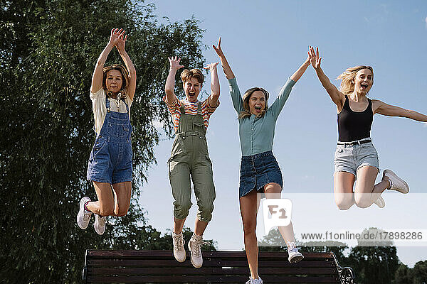 Happy friends jumping together in front of sky at park