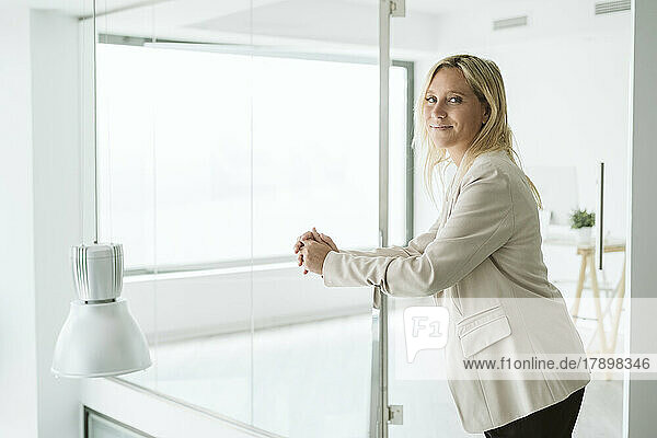 Businesswoman leaning on railing in minimalist office corridor