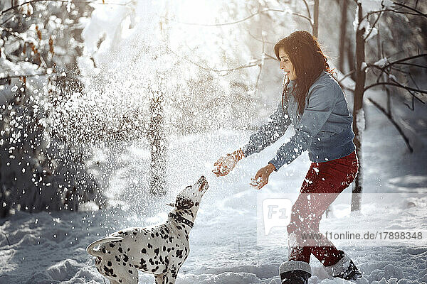Verspielte Frau mit Dalmatiner im Schnee im Park