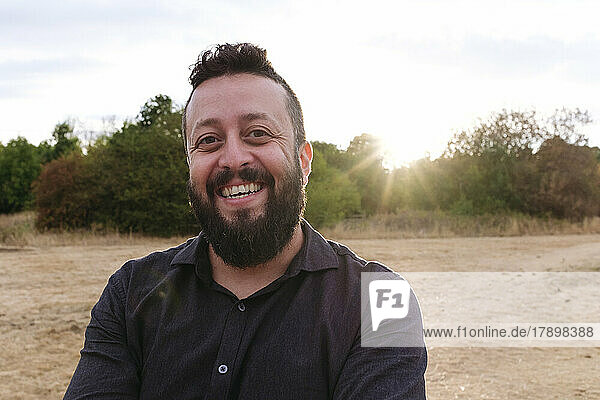 Happy mature man with beard in field at sunset
