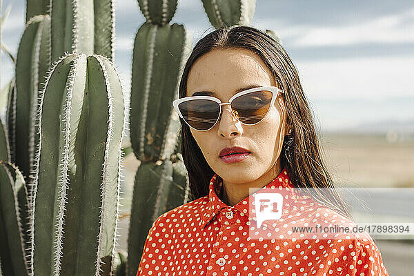Confident young woman with sunglasses standing in front of cactus plant
