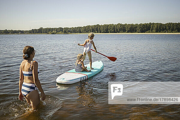 Girls having fun on paddleboard with mother at lake