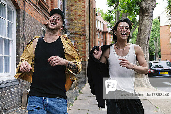 Happy gay couple running together on sidewalk in city