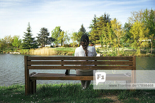 Young woman sitting on bench in front of lake at park