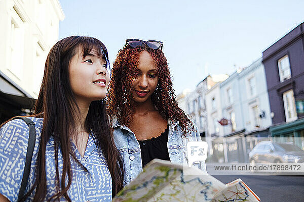 Smiling young woman with friend holding map standing on street
