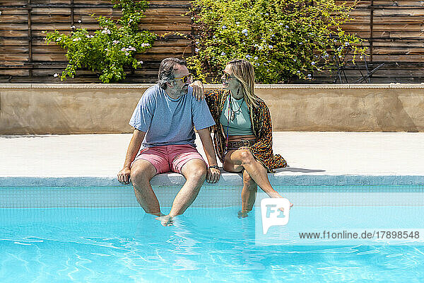 Happy mature couple sitting by pool on sunny day