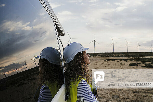 Engineer wearing hardhat leaning on van at wind farm