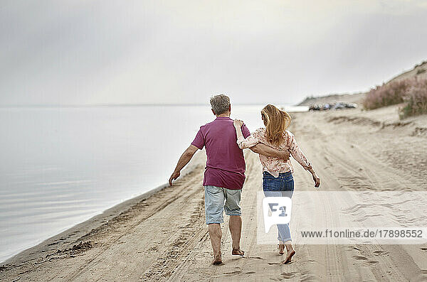 Father and daughter walking together on sand at sunset