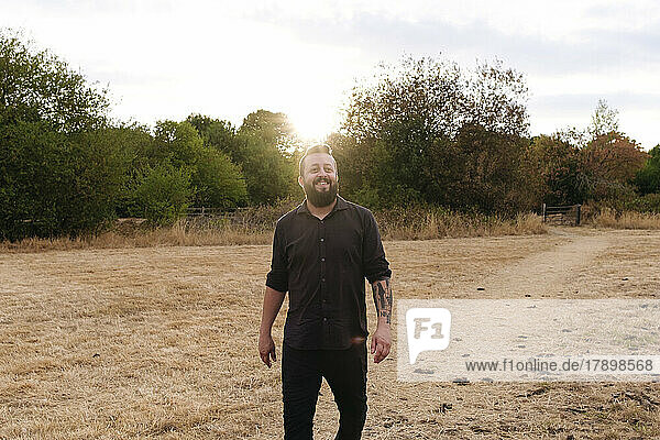 Reifer lächelnder Mann  der bei Sonnenuntergang im Feld spaziert