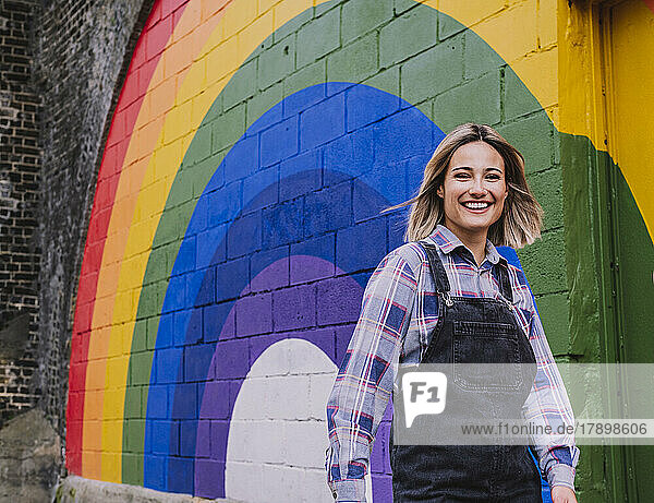 Happy young woman walking by rainbow mural on wall