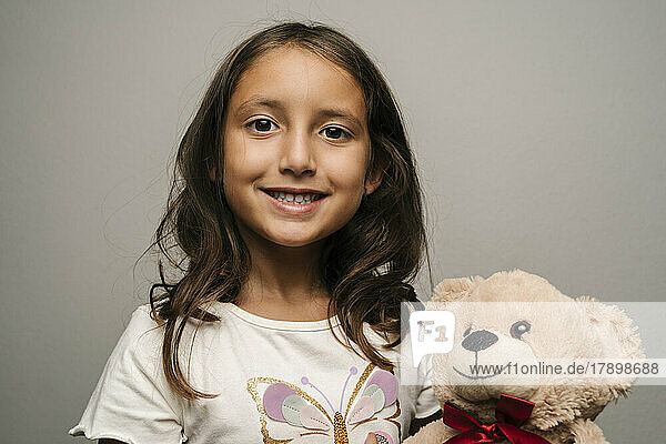 Smiling girl with teddy bear against gray background