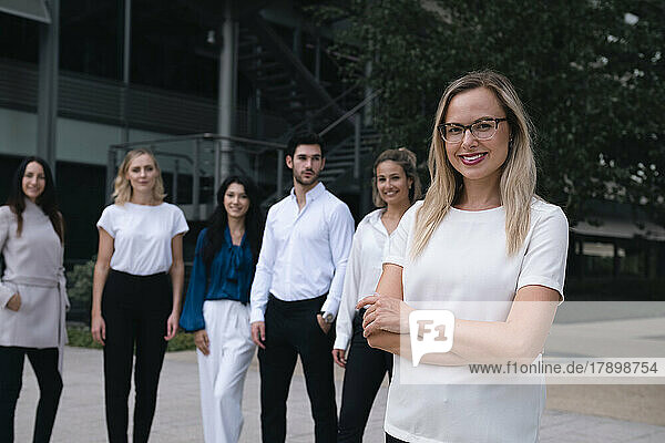 Smiling businesswoman standing with arms crossed in front of colleague at office park