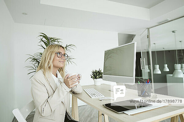 Businesswoman sitting at desk in office holding cup of coffee
