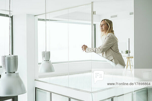 Businesswoman leaning on railing in minimalist office corridor