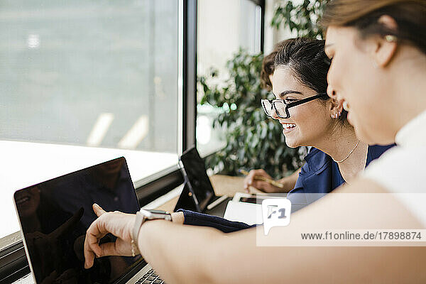 Glückliche Geschäftsfrau zeigt von einem Kollegen im Büro auf den Laptop