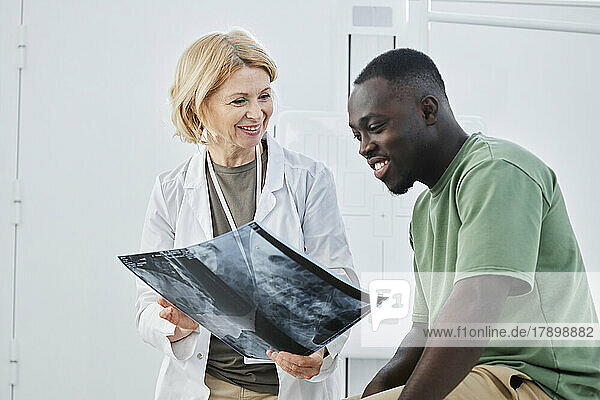 Smiling doctor holding X-ray looking at patient in clinic