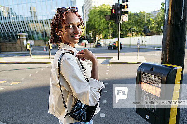 Lächelnde Frau wartet am Fußgängerüberweg-Knopf