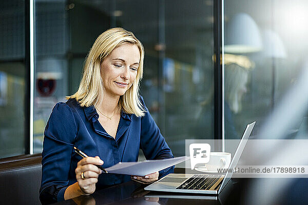 Lächelnde reife Geschäftsfrau erledigt Papierkram im Café