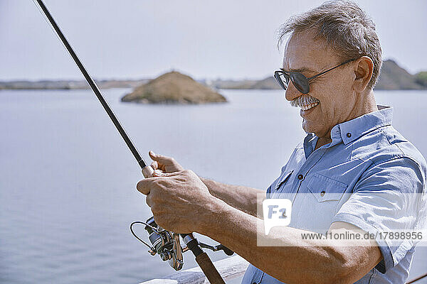 Happy senior man with fishing rod standing by sea