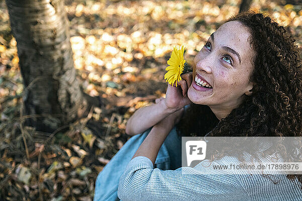 Glückliche junge Frau mit gelber Blume sitzt im Park