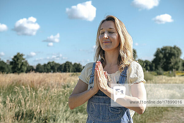 Smiling mature woman with hands clasped praying on sunny day